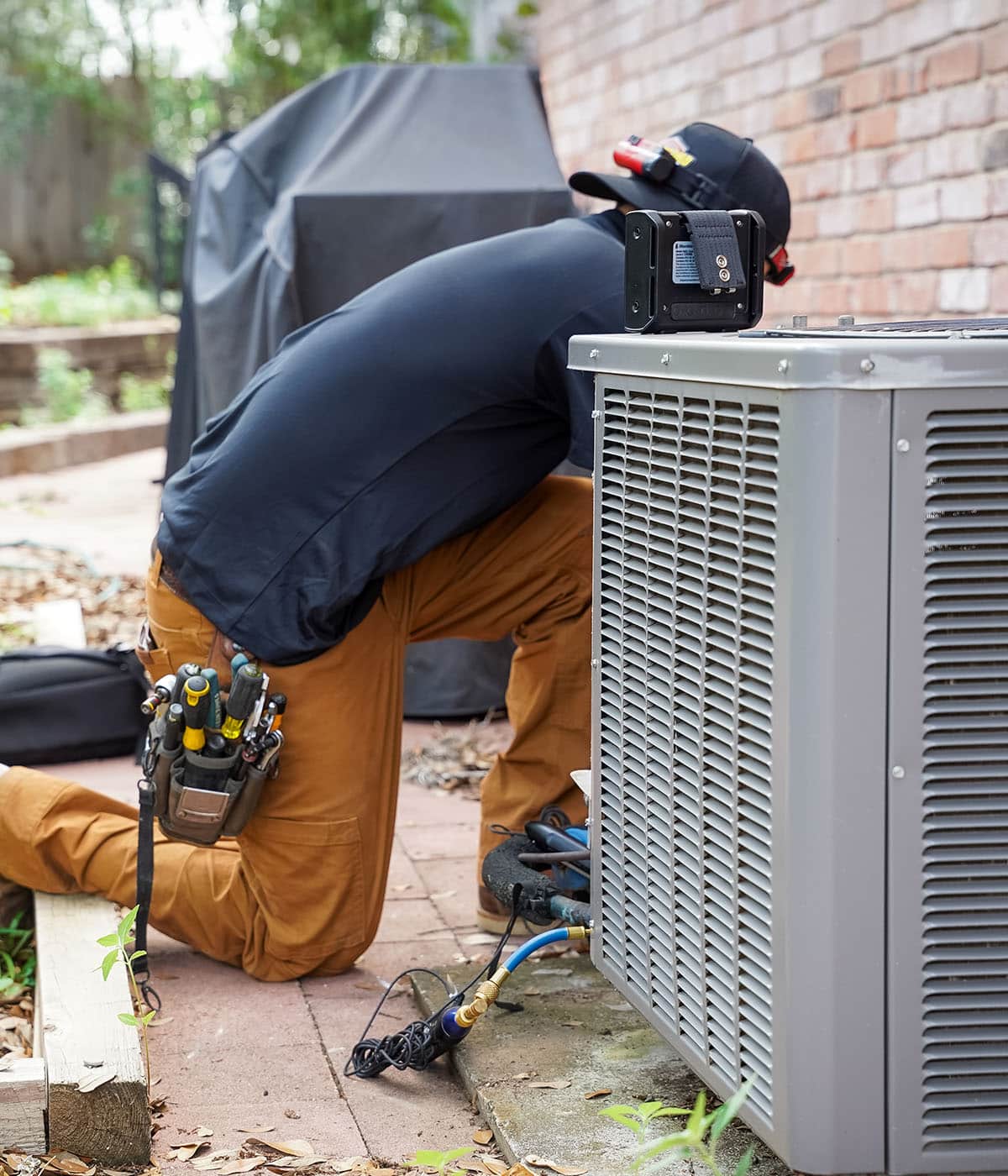 HVAC technician kneeling while repairing an air conditioning unit in a residential setting.