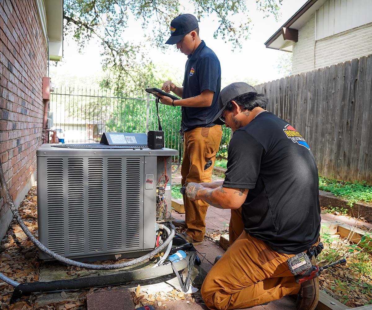 Two Honeycomb HVAC technicians working on an air conditioning unit in a residential backyard.