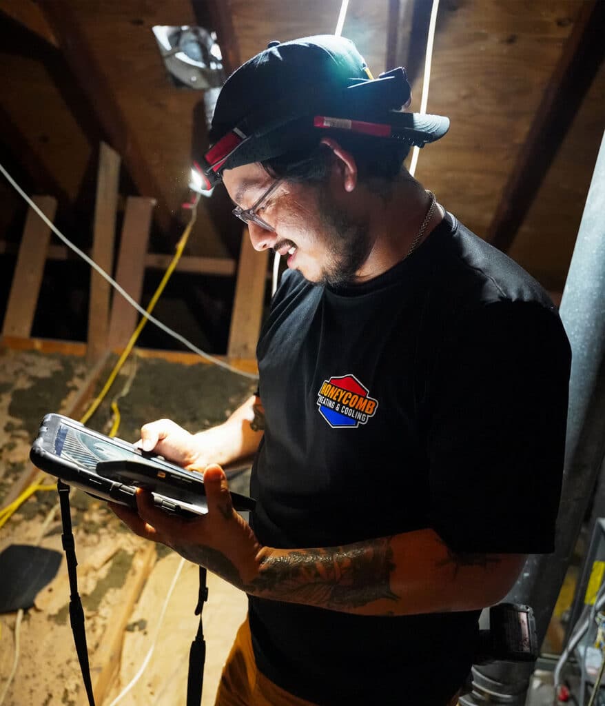HVAC maintenance work being performed in an attic with a technician using a tablet