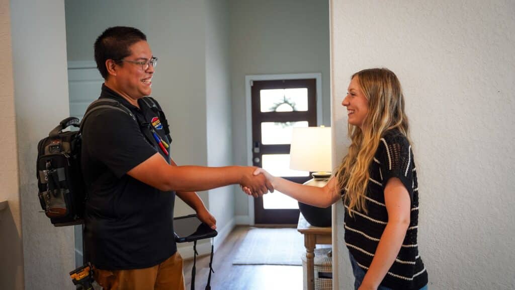 Home service technician in uniform shaking hands with a satisfied female customer in the brightly lit entryway of her house after solving AC repair mistakes.