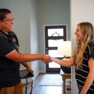 Best AC Repair: Home service technician in uniform shaking hands with a satisfied female customer in the brightly lit entryway of her house after solving AC repair mistakes.