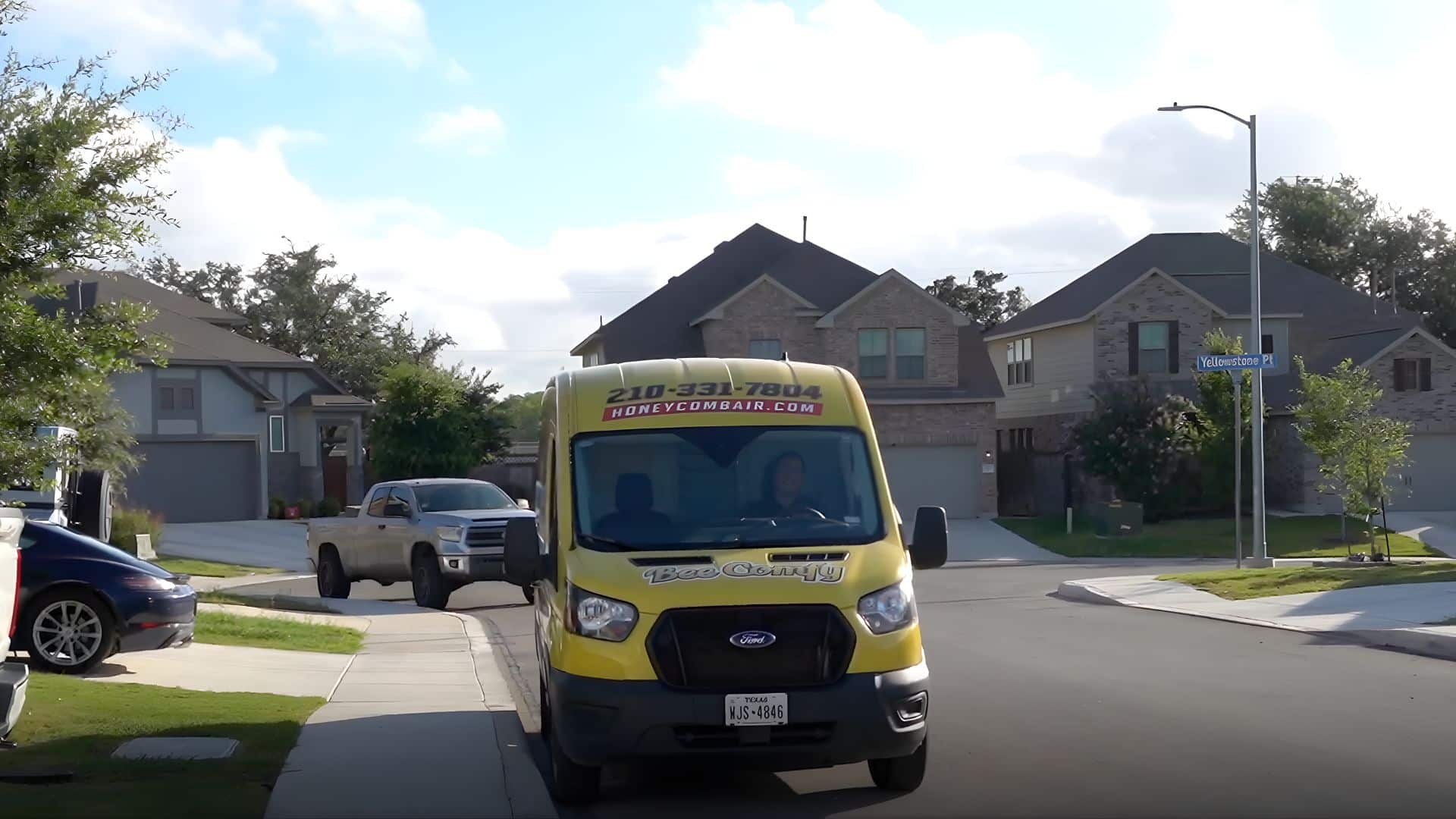 A clear shot of a brightly branded yellow Honeycomb Heating & Cooling service van driving through a suburban neighborhood. The easily recognizable vehicle promotes the company's local presence and reliability, suggesting to customers that they are dealing with one of the most visible and dependable (best HVAC contractors) in the area.
