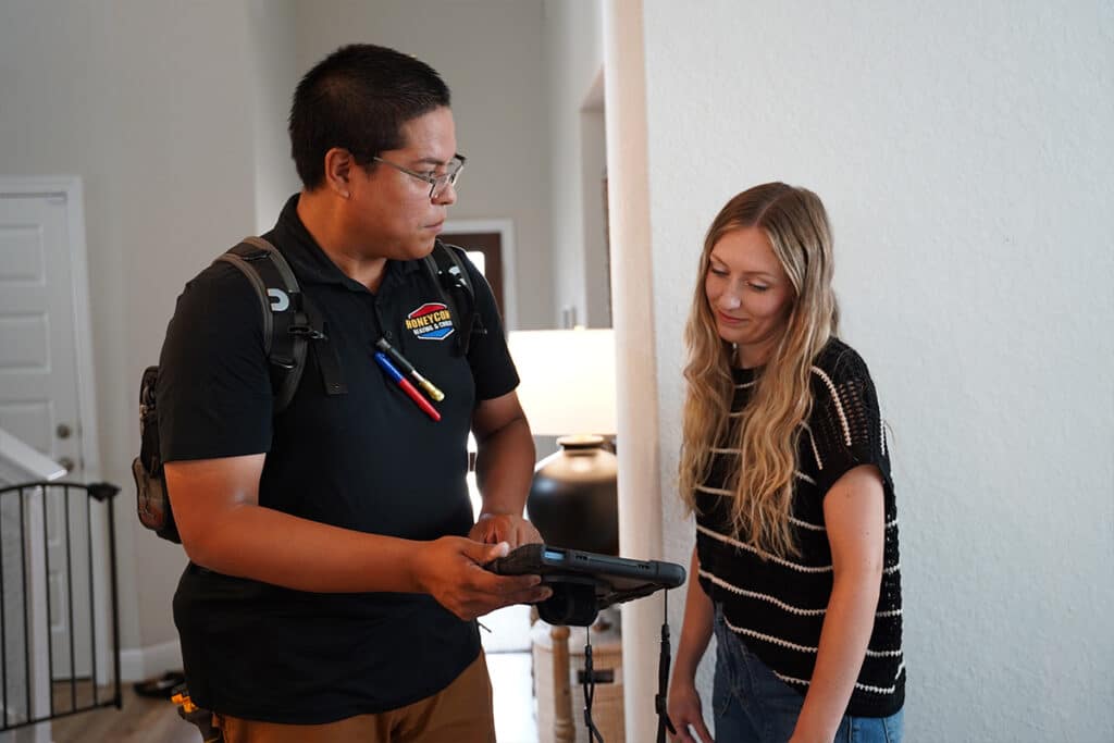 Honeycomb Heating & Cooling technician reviewing service details on a tablet with a homeowner inside a San Antonio home.