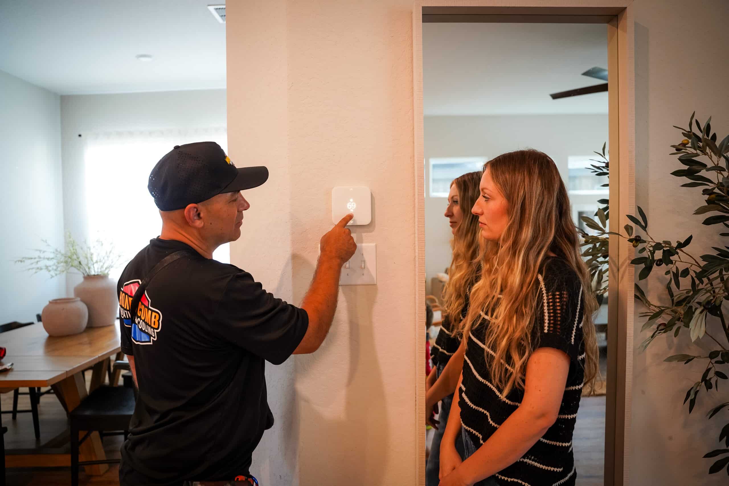 HVAC technician inspecting and setting up a wall-mounted smart thermostat with a homeowner. Smart Thermostat Installation Services