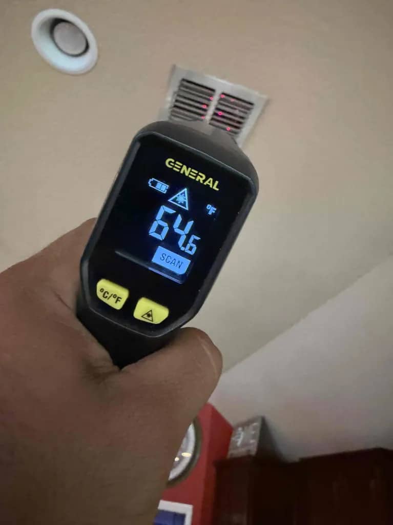 Infrared thermometer reading cool air output of 64.6°F from a ceiling vent during performance testing for two-stage vs inverter ac San Antonio, by Honeycomb.