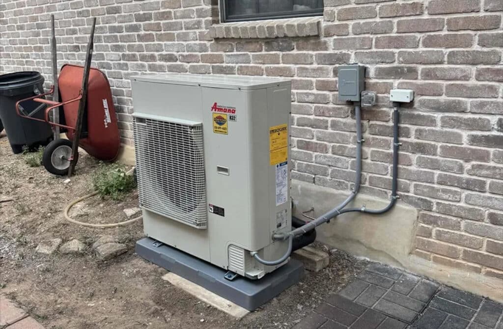 High-Efficiency Amana Unit Installation | Inverter AC Cost San Antonio | Honeycomb An Amana S-Series side-discharge inverter AC unit installed on a composite pad against a brick wall, providing a modern comfort solution affecting inverter AC cost San Antonio, by Honeycomb.